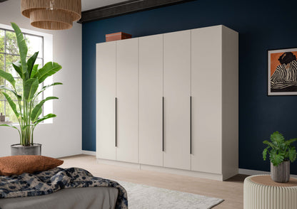 Kleiderschrank in Weiß mit langen Griffen, freistehend im Raum mit Textilien und Pflanze