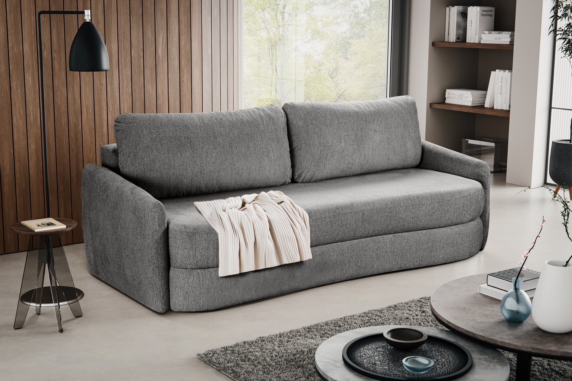 Schlafsofa mit grauem Polsterstoff, Decke auf der Sitzfläche, zwei Rückenkissen